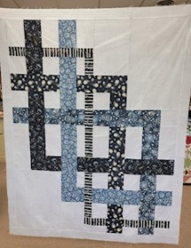 Quilt top with white background and ribbons of blue glow in the dark fabric intertwined.